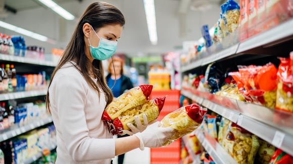 Buyer wearing a protective mask.Shopping during the pandemic quarantine.Nonperishable smart purchased household pantry groceries preparation.Woman buying few pasta packages.Budget pastas and noodles.